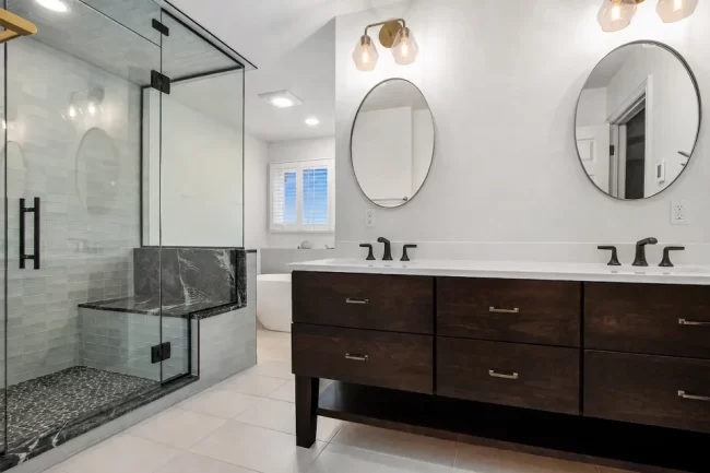 Spacious Bathroom with Glass Shower and Storage Cabinet | Pennings & Sons Spacious bathroom with glass shower enclosure, pale green storage cabinet, tile flooring, window, and soft blue-green trim