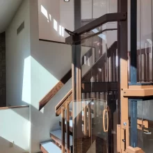 Close-up view of a custom glass residential elevator integrated with wood stairs and warm interior finishes