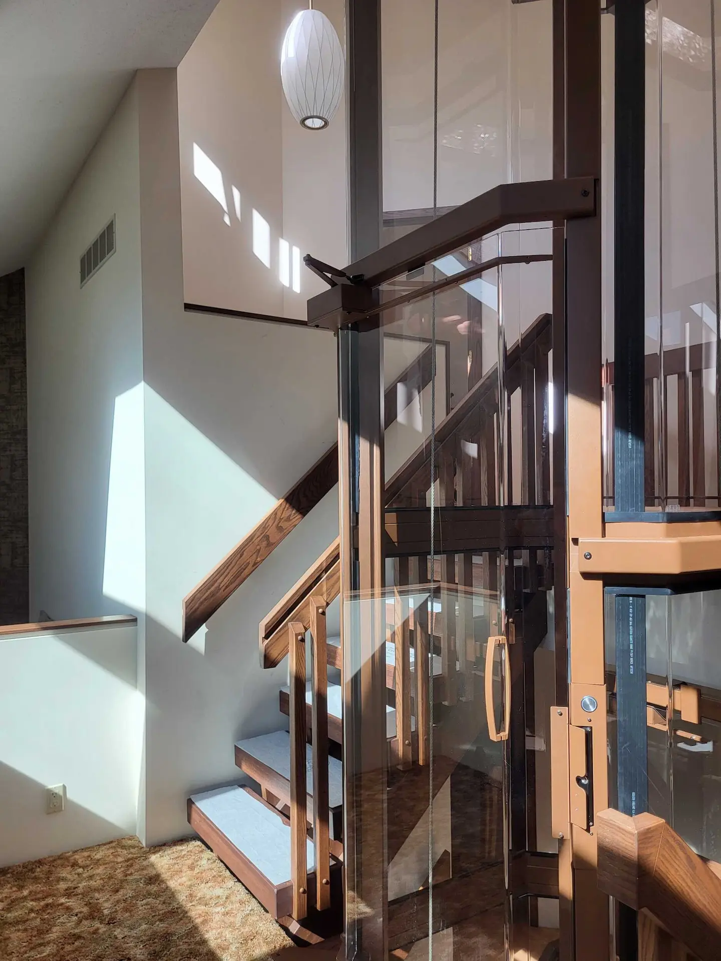 Close-up view of a custom glass residential elevator integrated with wood stairs and warm interior finishes