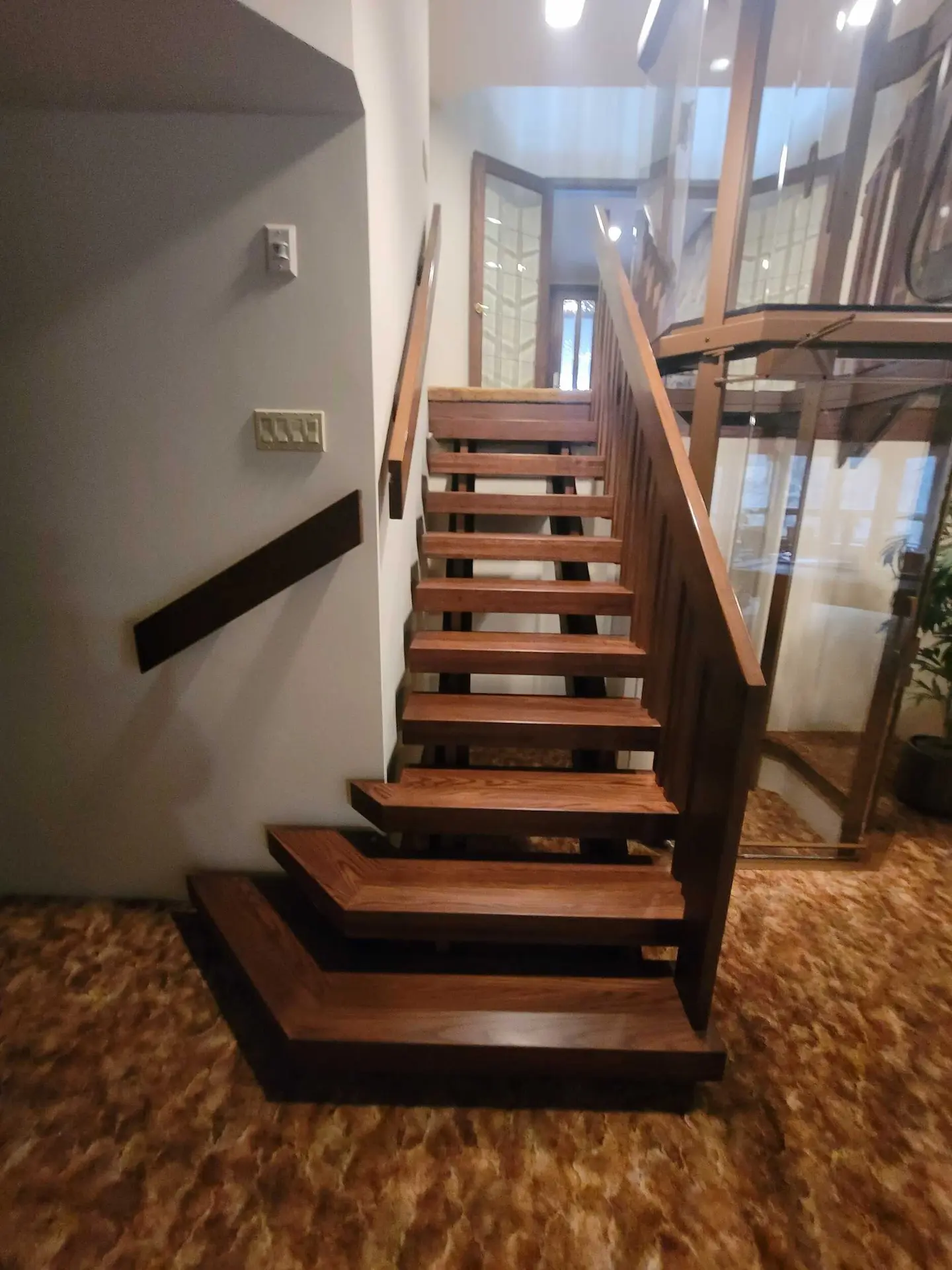 Custom wood stair treads installed beside a residential elevator with glass enclosure and warm interior finishes