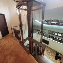 Glass elevator shaft installed beside a wood staircase with warm carpet, railings, and multi-level access.