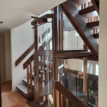 Glass home elevator beside a custom wood staircase, viewed from the upper landing of a multi-level residence