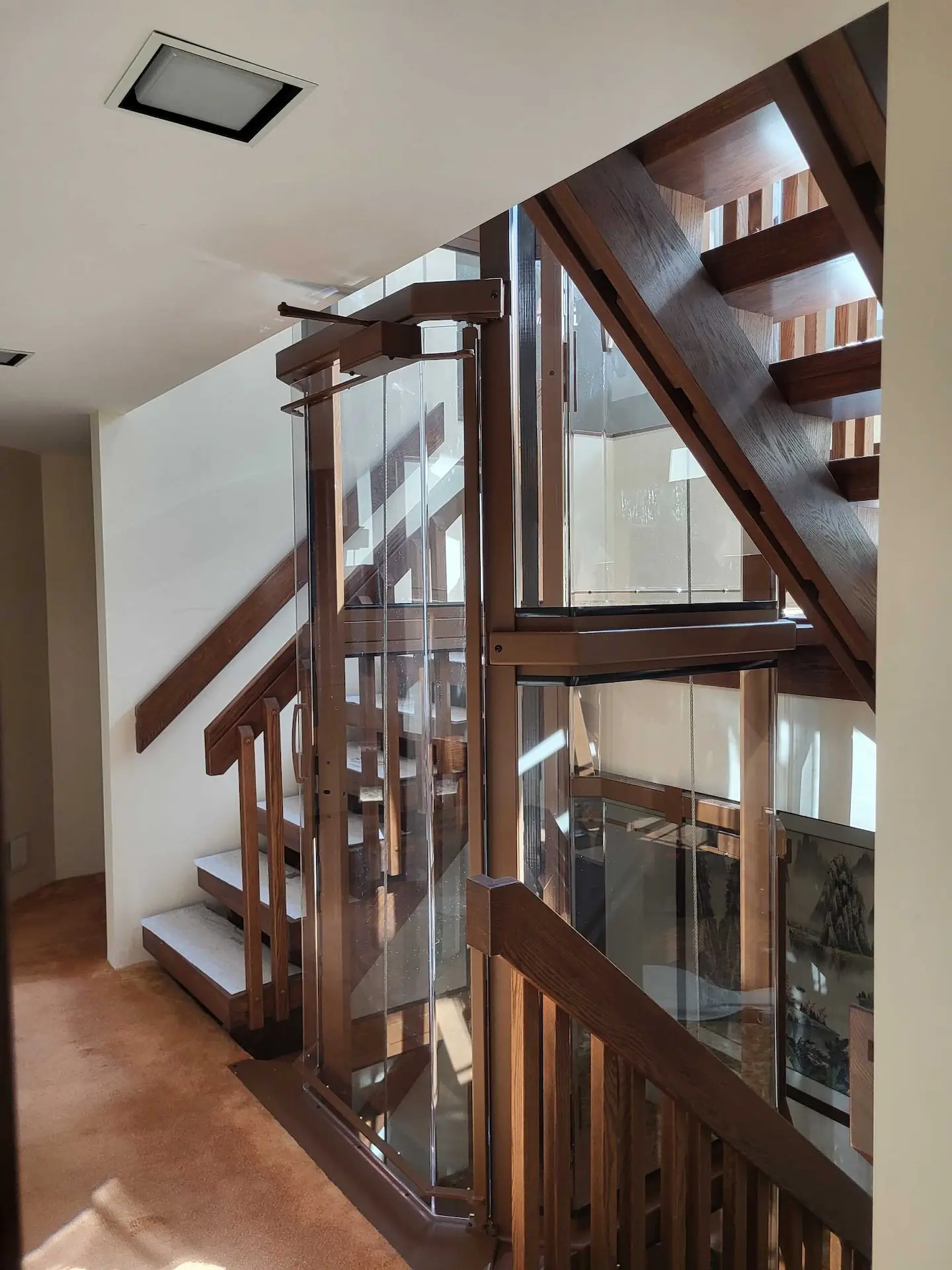 Glass home elevator beside a custom wood staircase, viewed from the upper landing of a multi-level residence