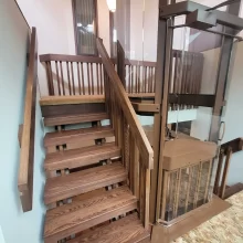 Home elevator positioned at a staircase landing with wood railings, glass panels, and carpeted floor area.