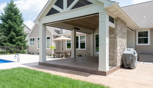 Covered outdoor living area next to the pool with stone fireplace, patio space, and white columns
