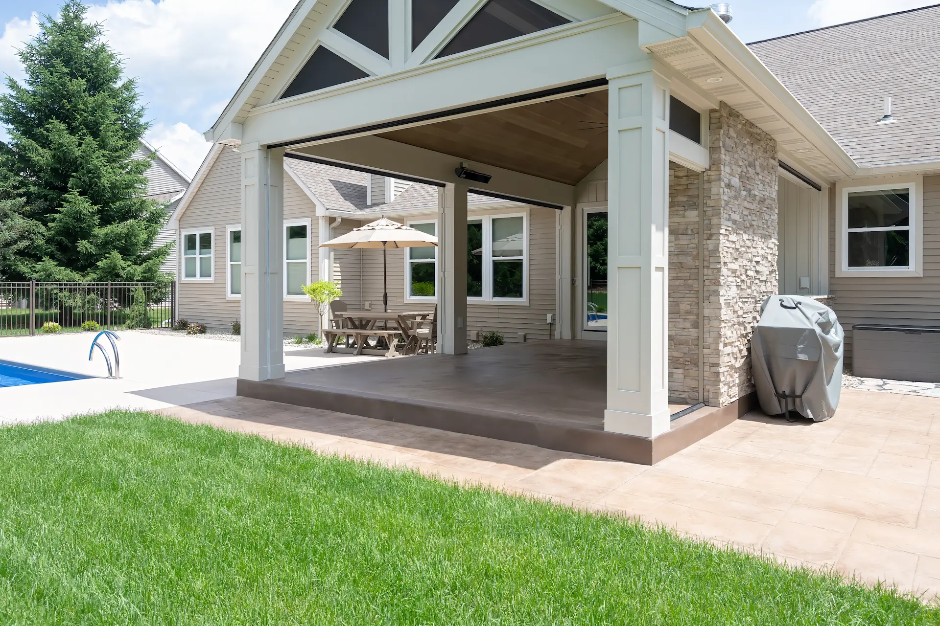 Covered outdoor living area next to the pool with stone fireplace, patio space, and white columns