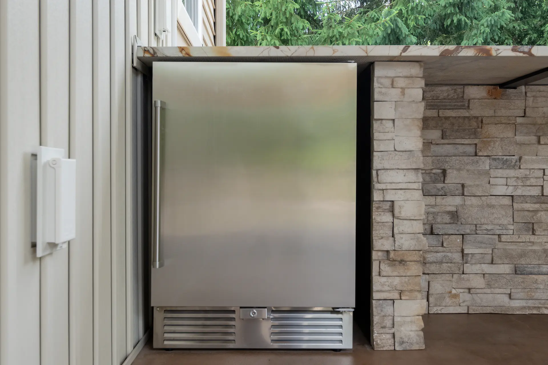 Stainless outdoor refrigerator built into the covered patio next to a stone counter wall