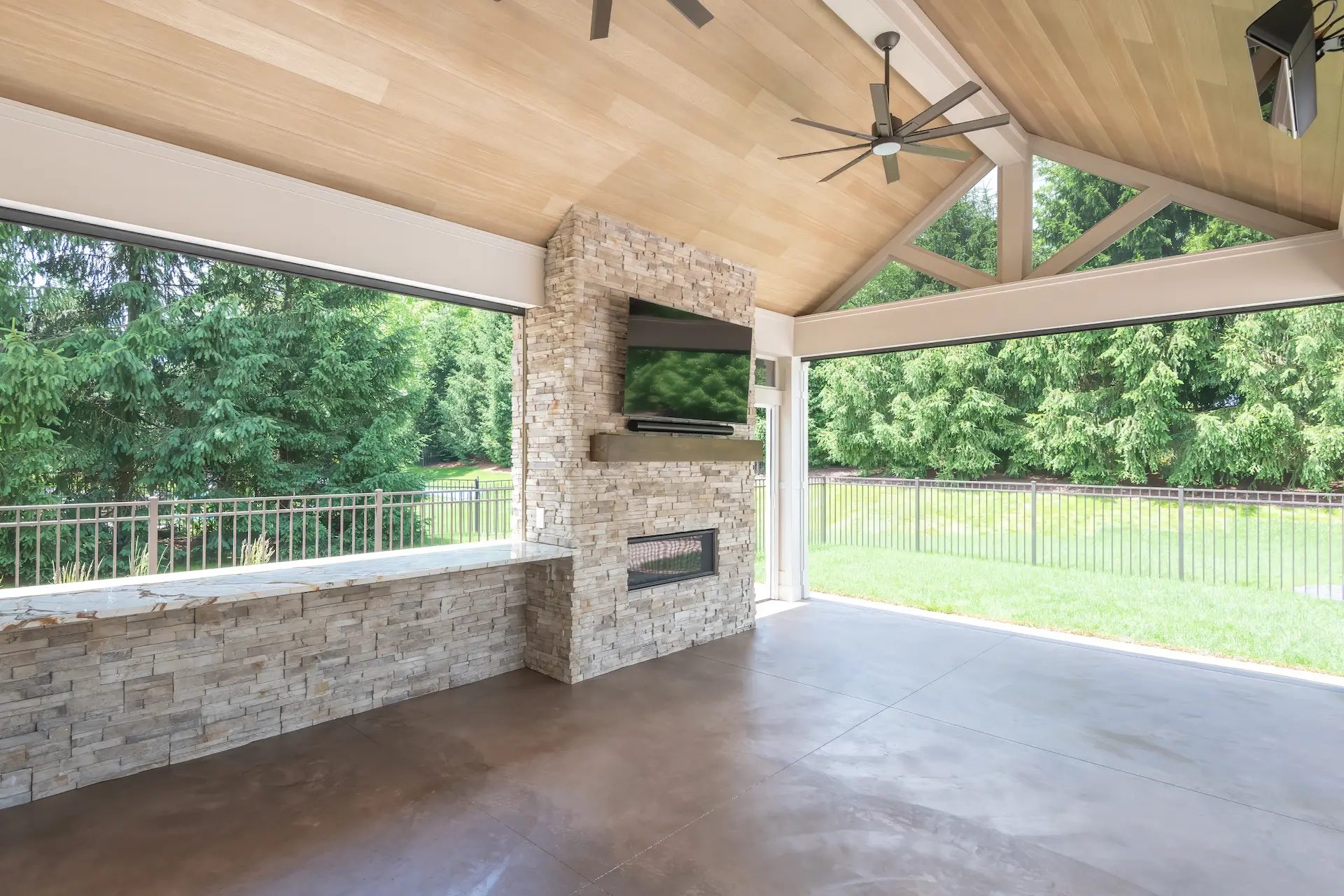 Stone fireplace wall with mounted TV inside a covered backyard patio
