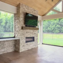 Stone fireplace feature with mounted TV, wood look ceiling, and large screened patio openings.
