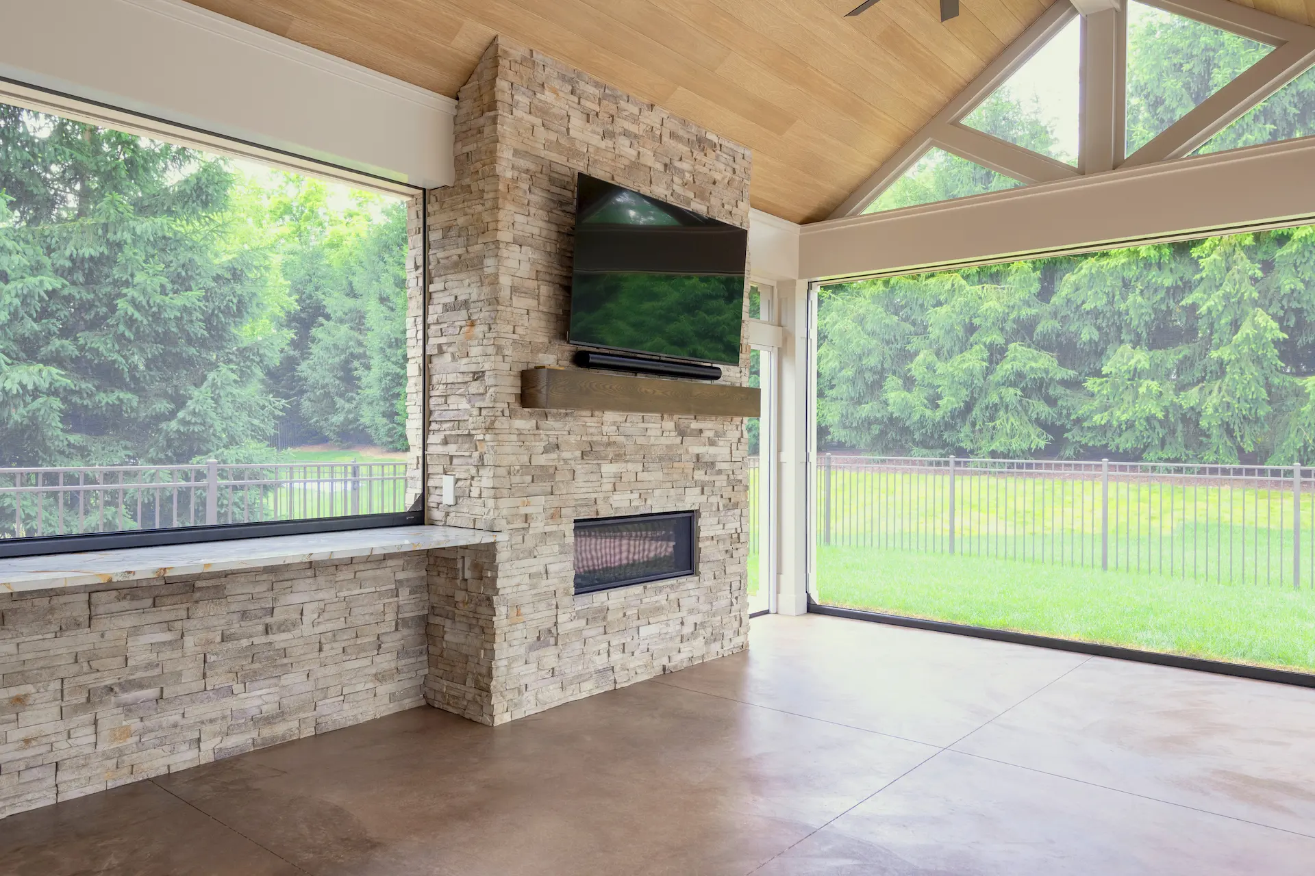 Stone fireplace feature with mounted TV, wood look ceiling, and large screened patio openings.