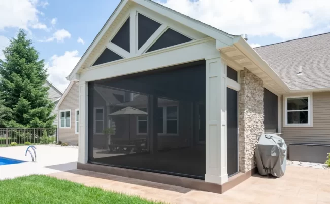 Outdoor Fireplace with Retractable Screens | Pennings & Sons Stone fireplace and TV wall inside the covered patio with retractable screens around the space.