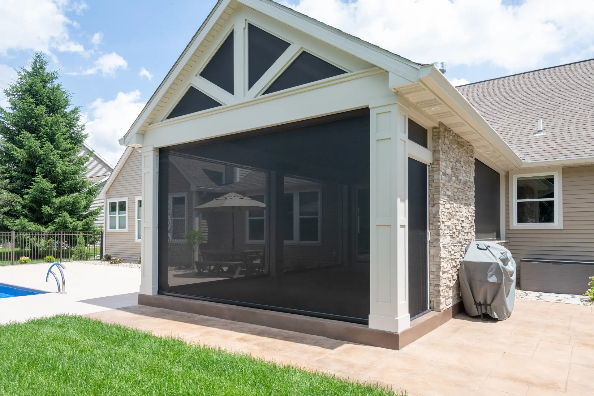 Stone fireplace and TV wall inside the covered patio with retractable screens around the space.