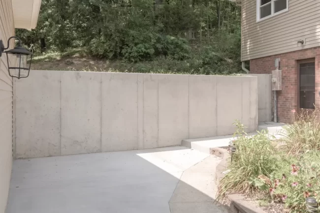 Concrete Retaining Wall Beside Garage Rebuild | Pennings & Sons Finished concrete retaining wall and driveway area beside a rebuilt garage with landscaping and nearby home exterior
