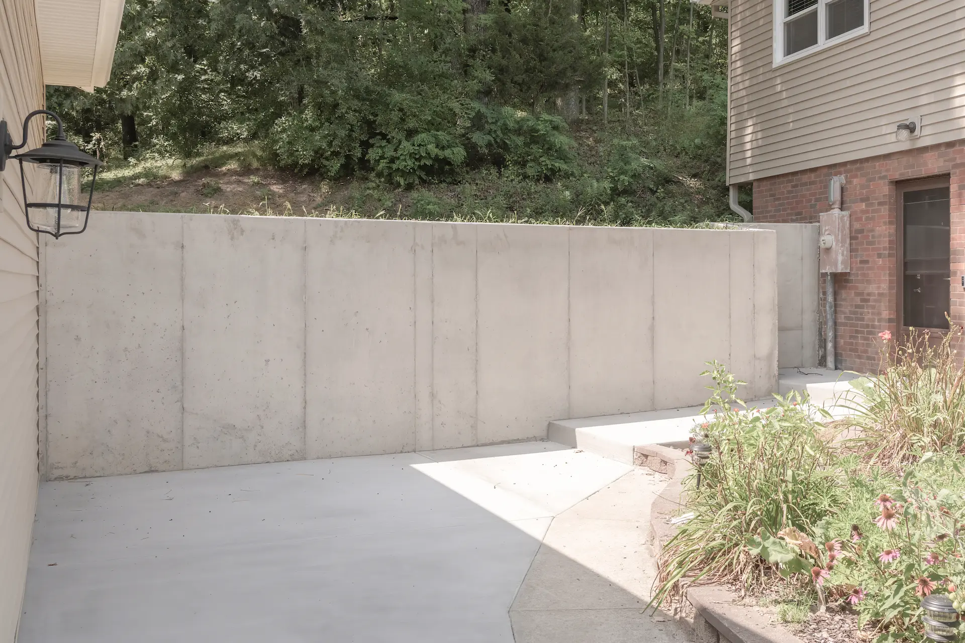 Finished concrete retaining wall and driveway area beside a rebuilt garage with landscaping and nearby home exterior