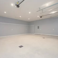 Finished rebuilt garage interior with gray walls, white service door, recessed lighting, overhead door tracks, and smooth concrete floor