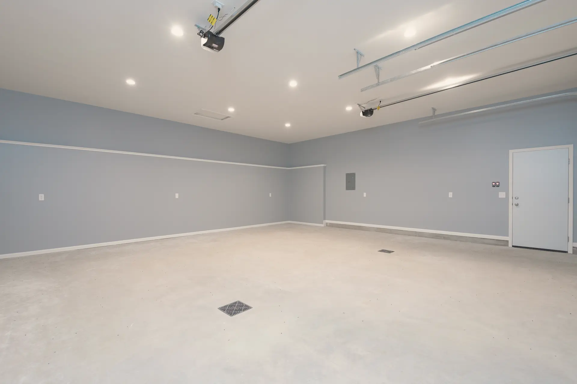 Finished rebuilt garage interior with gray walls, white service door, recessed lighting, overhead door tracks, and smooth concrete floor