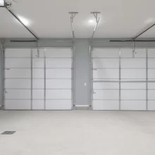 Interior view of two finished garage overhead doors with openers, gray walls, white trim, and clean concrete floor