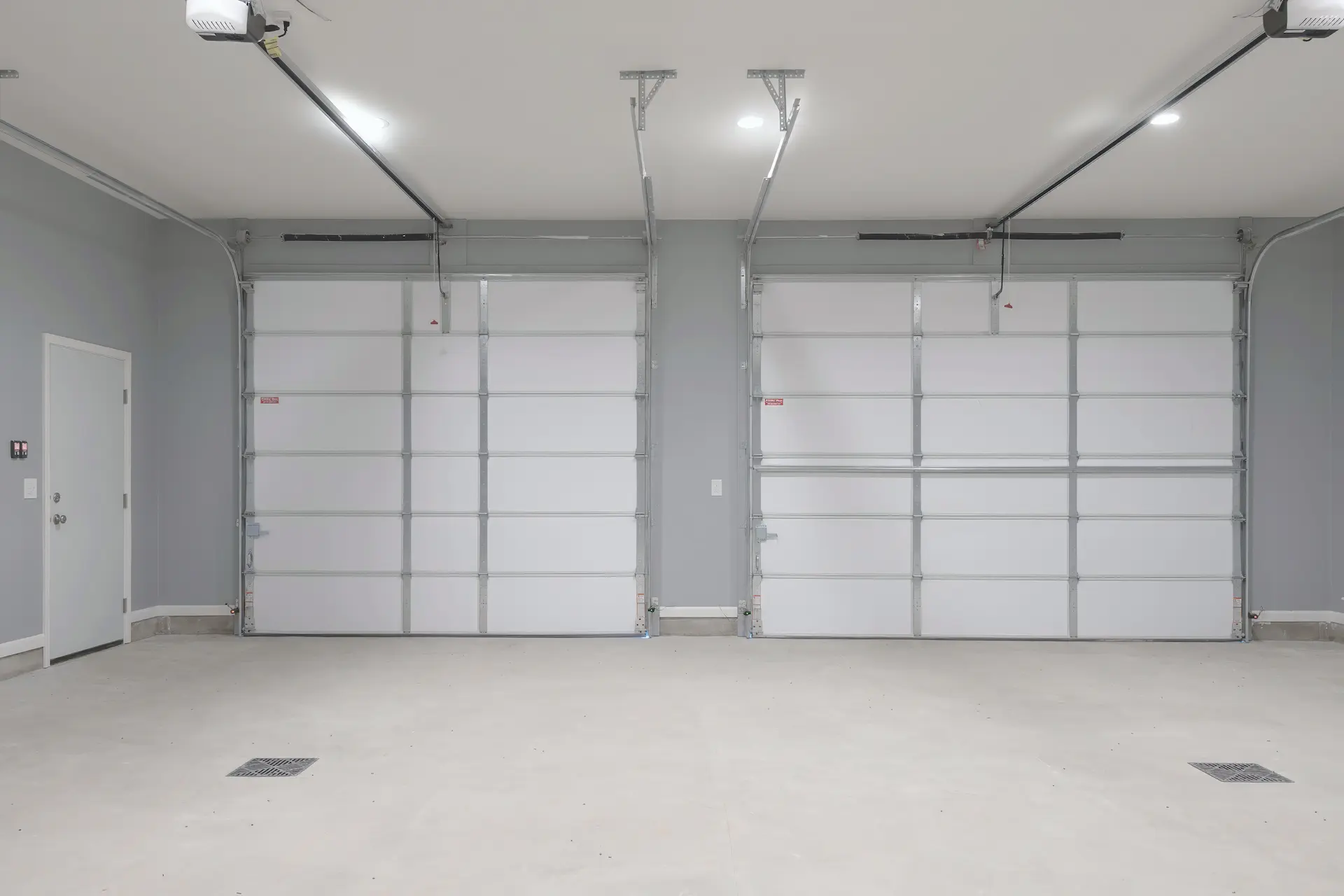 Interior view of two finished garage overhead doors with openers, gray walls, white trim, and clean concrete floor
