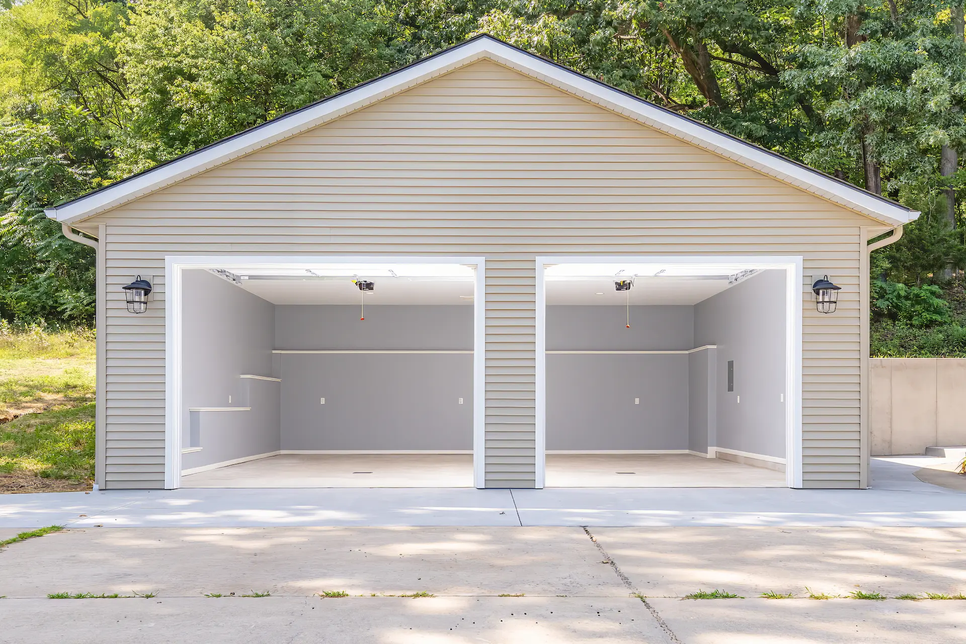 Finished rebuilt garage interior viewed from the driveway with open overhead doors, recessed lighting, gray walls, and white trim