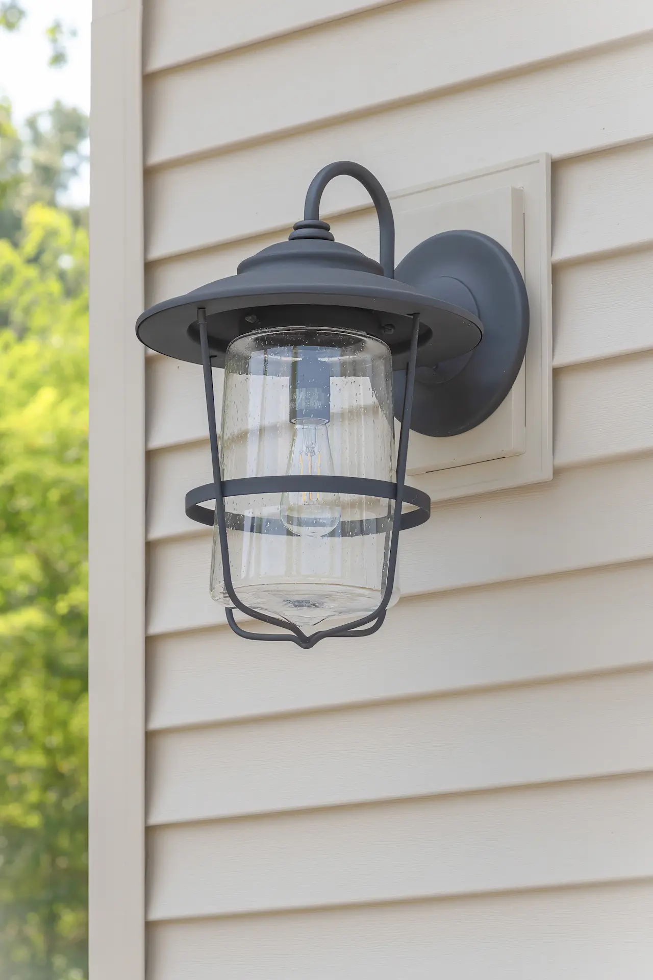 Close-up of a black exterior wall light installed on beige garage siding beside white trim