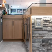 Close up of basement bar cabinetry, beverage fridge, stone face detail, and lighted display shelving