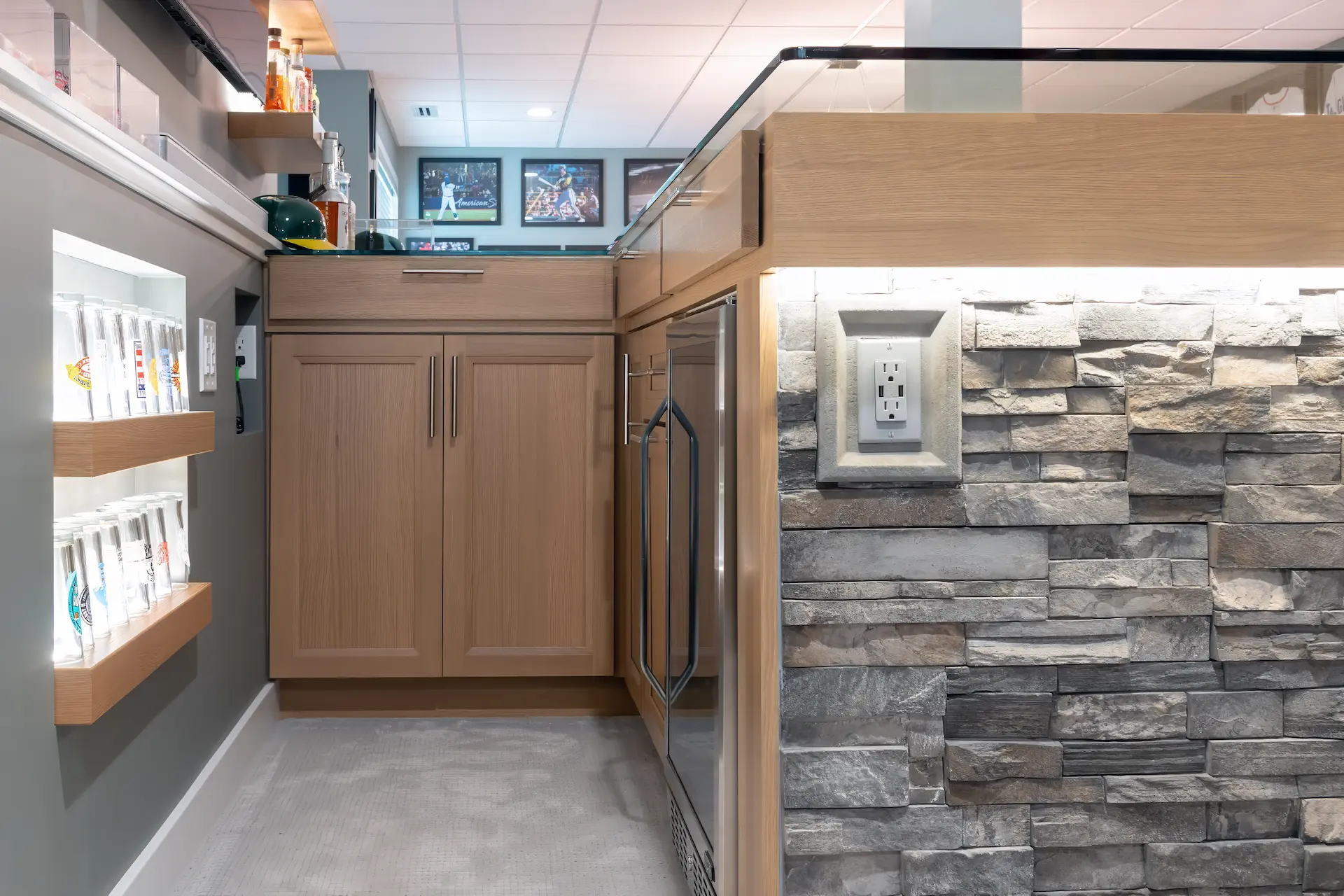 Close up of basement bar cabinetry, beverage fridge, stone face detail, and lighted display shelving