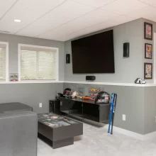 Basement media lounge with sectional seating, wall mounted TV, display shelves, and sports memorabilia
