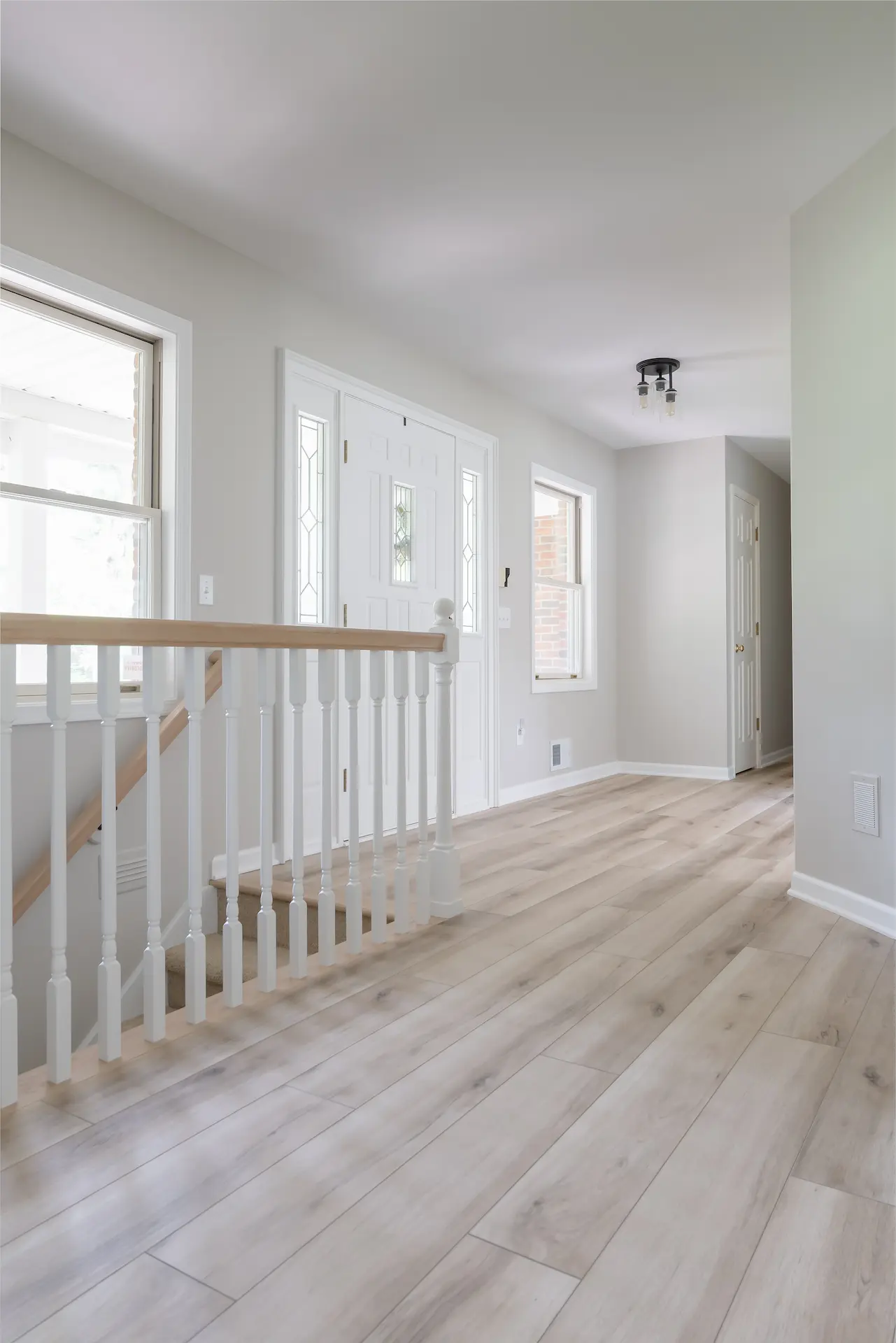 Updated entry hall with light wood flooring, white stair railing, and clean trim details