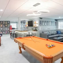 Finished basement game room with pool table, custom bar, lounge seating, and sports décor
