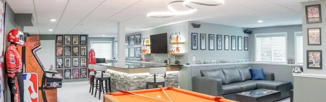 Finished basement game room with pool table, custom bar, lounge seating, and sports décor