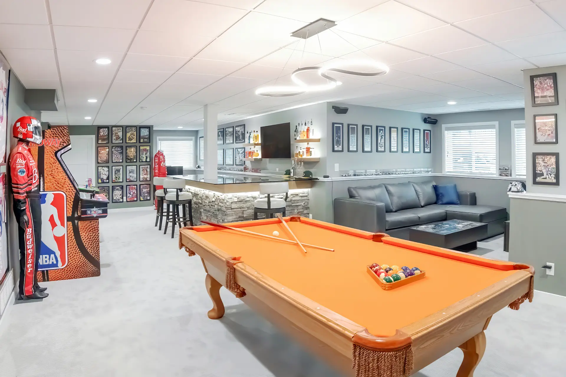 Finished basement game room with pool table, custom bar, lounge seating, and sports décor
