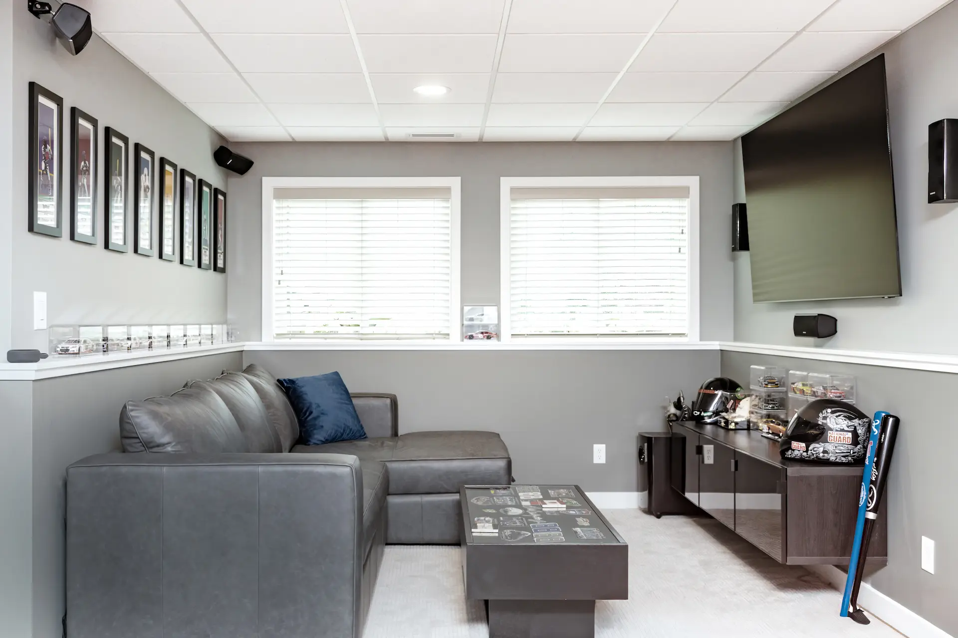 Finished basement TV room with gray walls, white trim, sectional seating, and display ledges