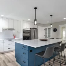 Blue kitchen island with bar seating, white perimeter cabinets, pendant lights, and stainless appliances