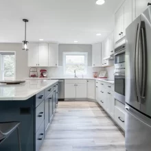 Remodeled kitchen with white cabinetry, blue island, stainless appliances, and light wood flooring