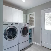 Laundry room with white storage cabinets, front-load washer and dryer, gray tile floor, and exterior door