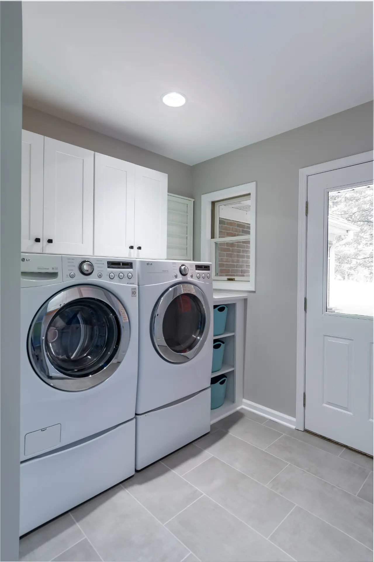 Laundry room with white storage cabinets, front-load washer and dryer, gray tile floor, and exterior door