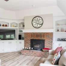 White built-in cabinetry and shelving surrounding a brick fireplace in a remodeled living room