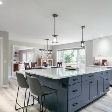 Bright remodeled kitchen with blue island, white cabinetry, dining area, and updated lighting
