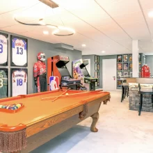 Sports themed basement with pool table, arcade games, framed jerseys, and custom bar seating