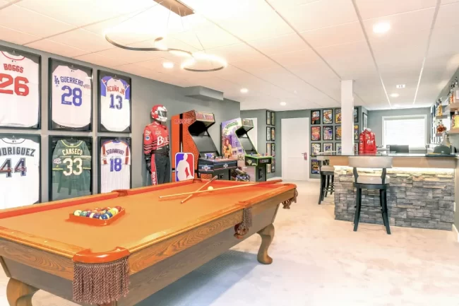 Sports Themed Basement Arcade Room | Pennings & Sons Sports themed basement with pool table, arcade games, framed jerseys, and custom bar seating