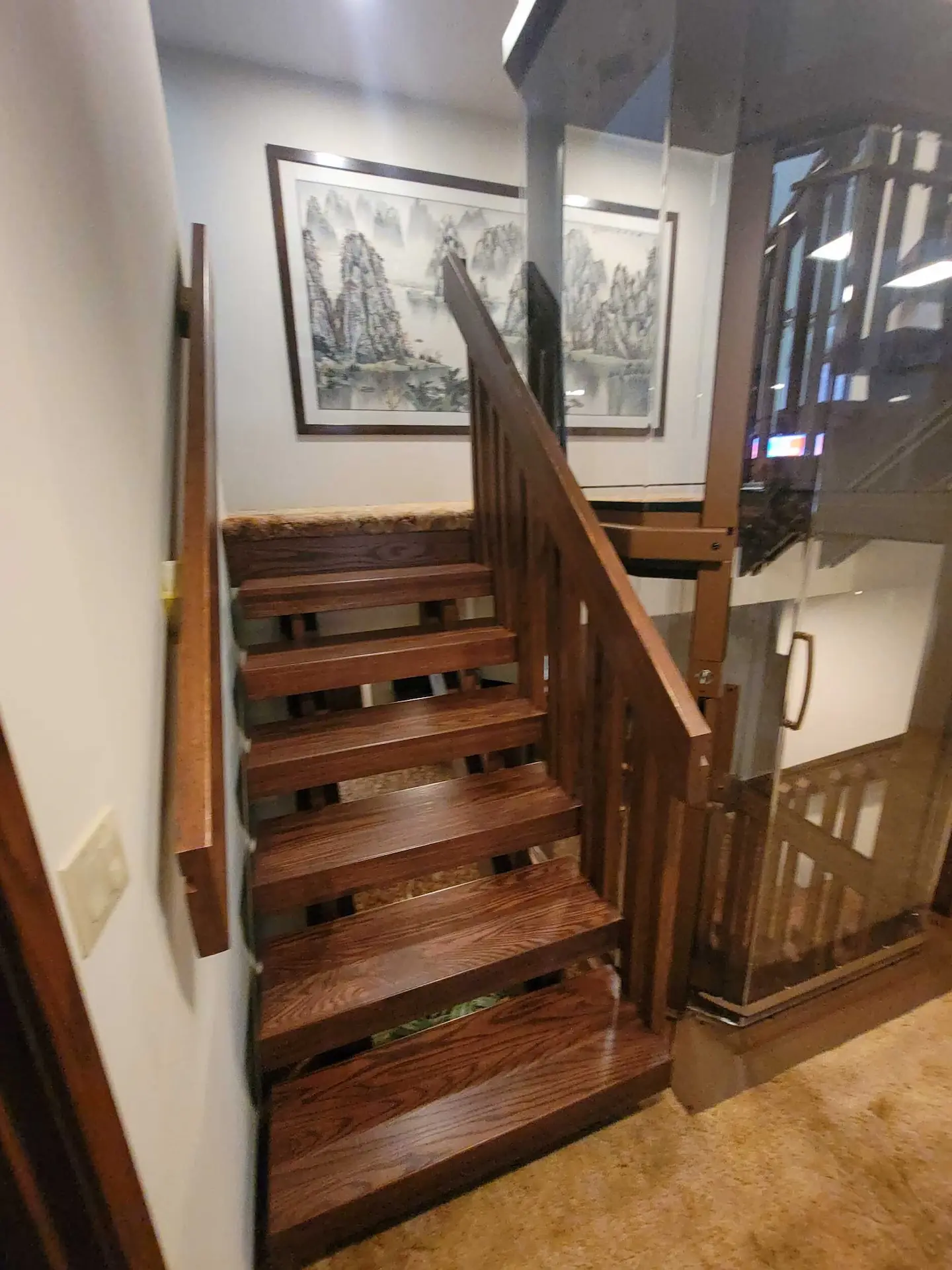 Finished wood stair treads next to a custom home elevator with glass panels and matching wood railings.